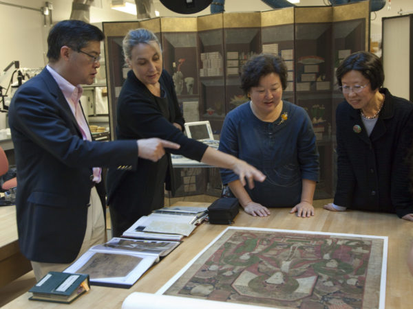 A group of conservators and curators study a painting.