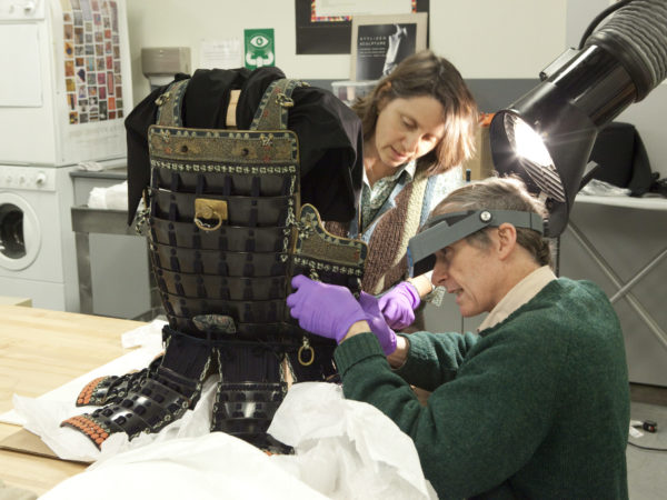 Two conservators repair a suit of armor.