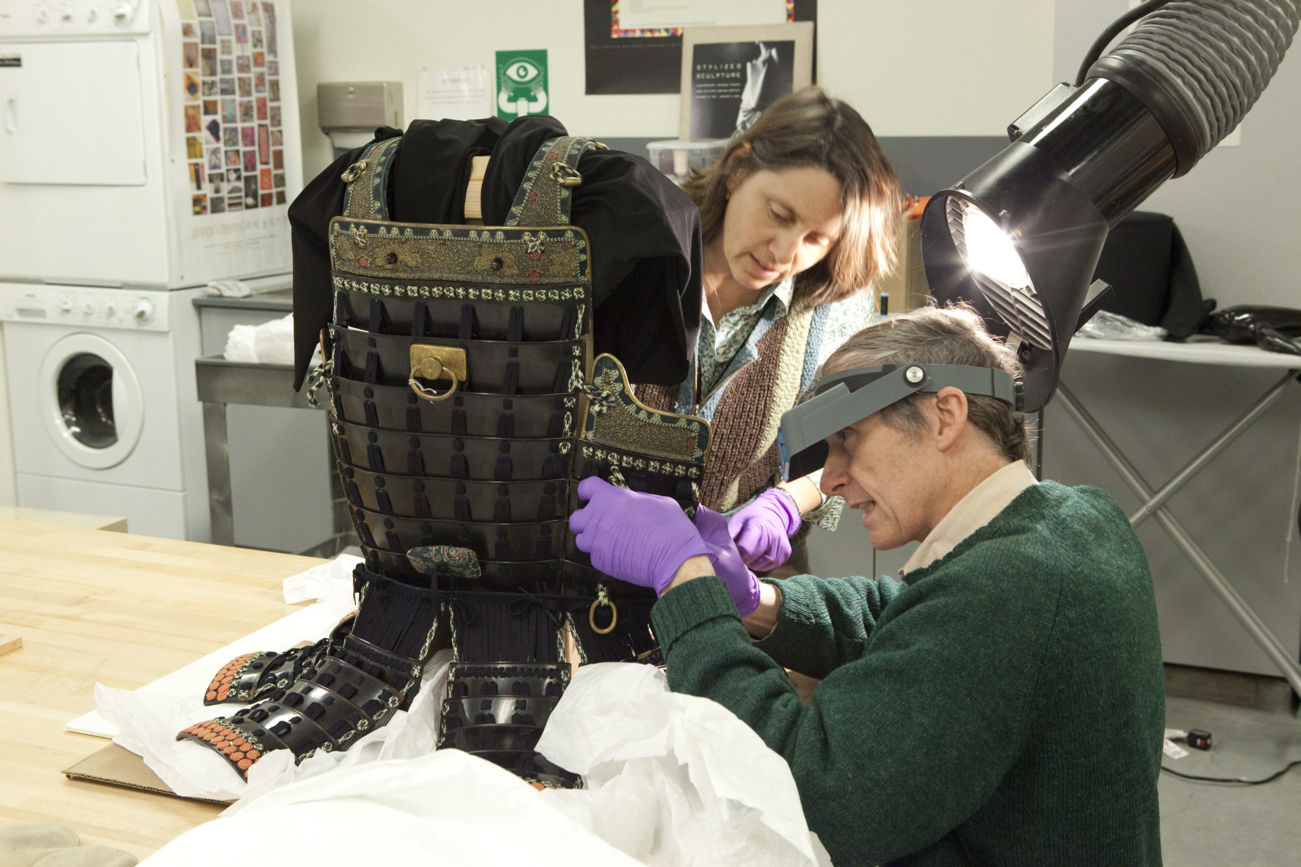Two conservators repair a suit of armor.
