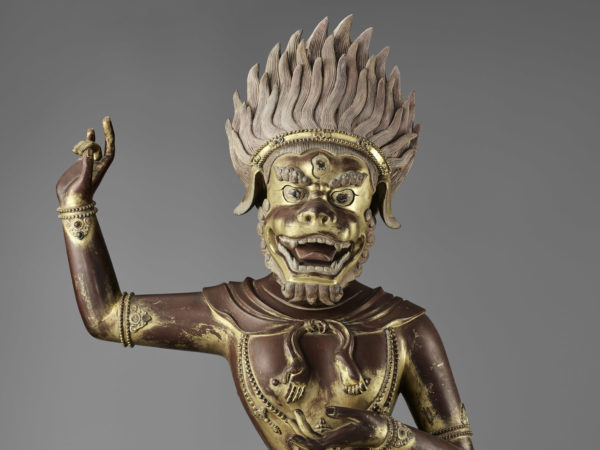 A figure of a Buddhist deity standing on its left leg and its right arm extended upward.