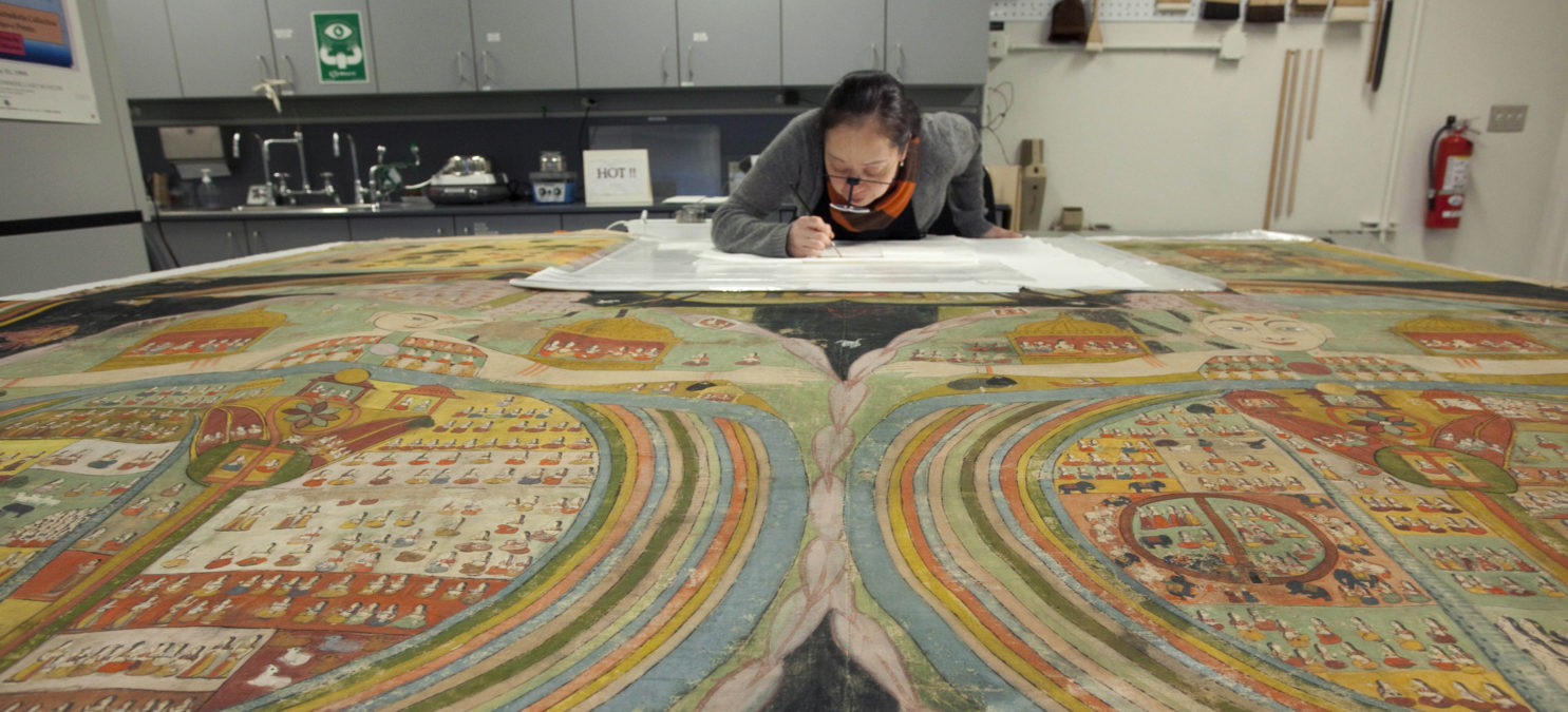 A conservator works on restoring a large artwork