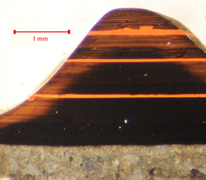 A fragment of lacquer ware examined in cross-section under the microscope proves to consist of over one hundred layers. The design is black, with three red stripes.