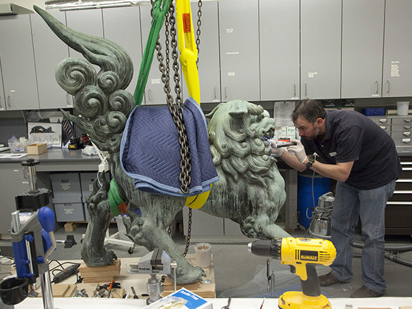 A conservator works on a bronze lion statue.