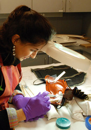 A conservator works on a suit of armor's face mask.