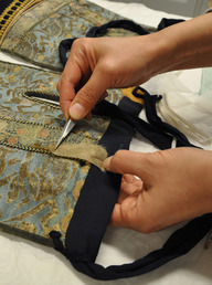 A conservator works on a suit of armor's thigh guards.