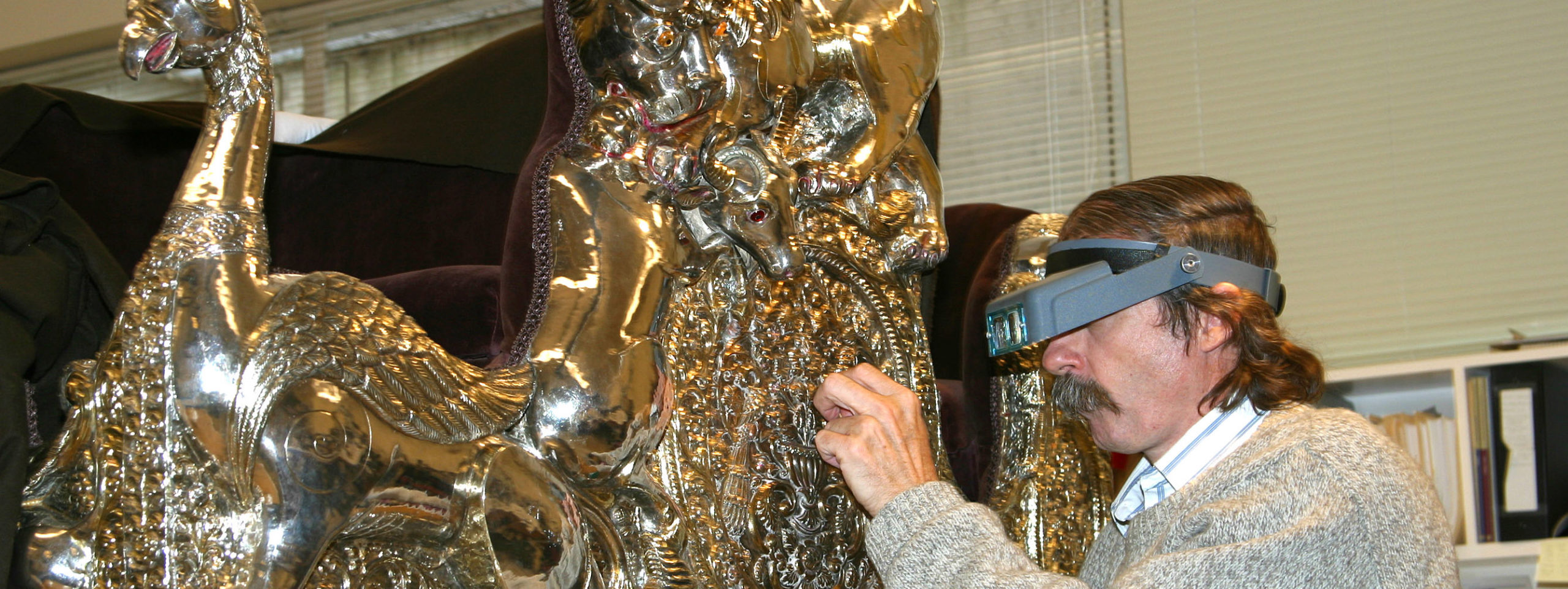 A conservator works on an elaborate silver howdah.